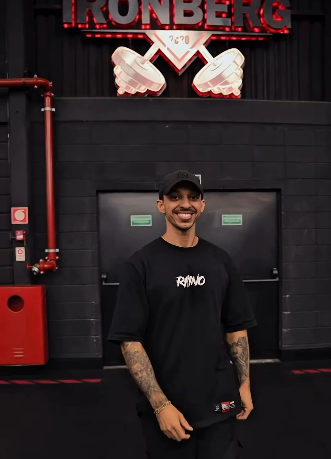 Kainã Soares sorrindo de corpo inteiro sob o letreiro do Ironberg