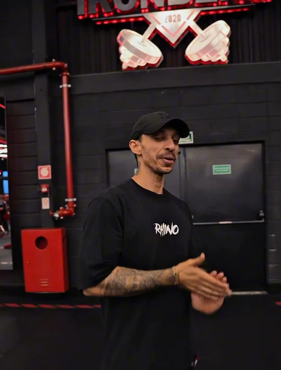 Kainã Soares explicando um exercício com as mãos, de boné e camiseta RHINO